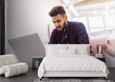 Casual young indian man using laptop with happy on sofa in modern office Wall mural